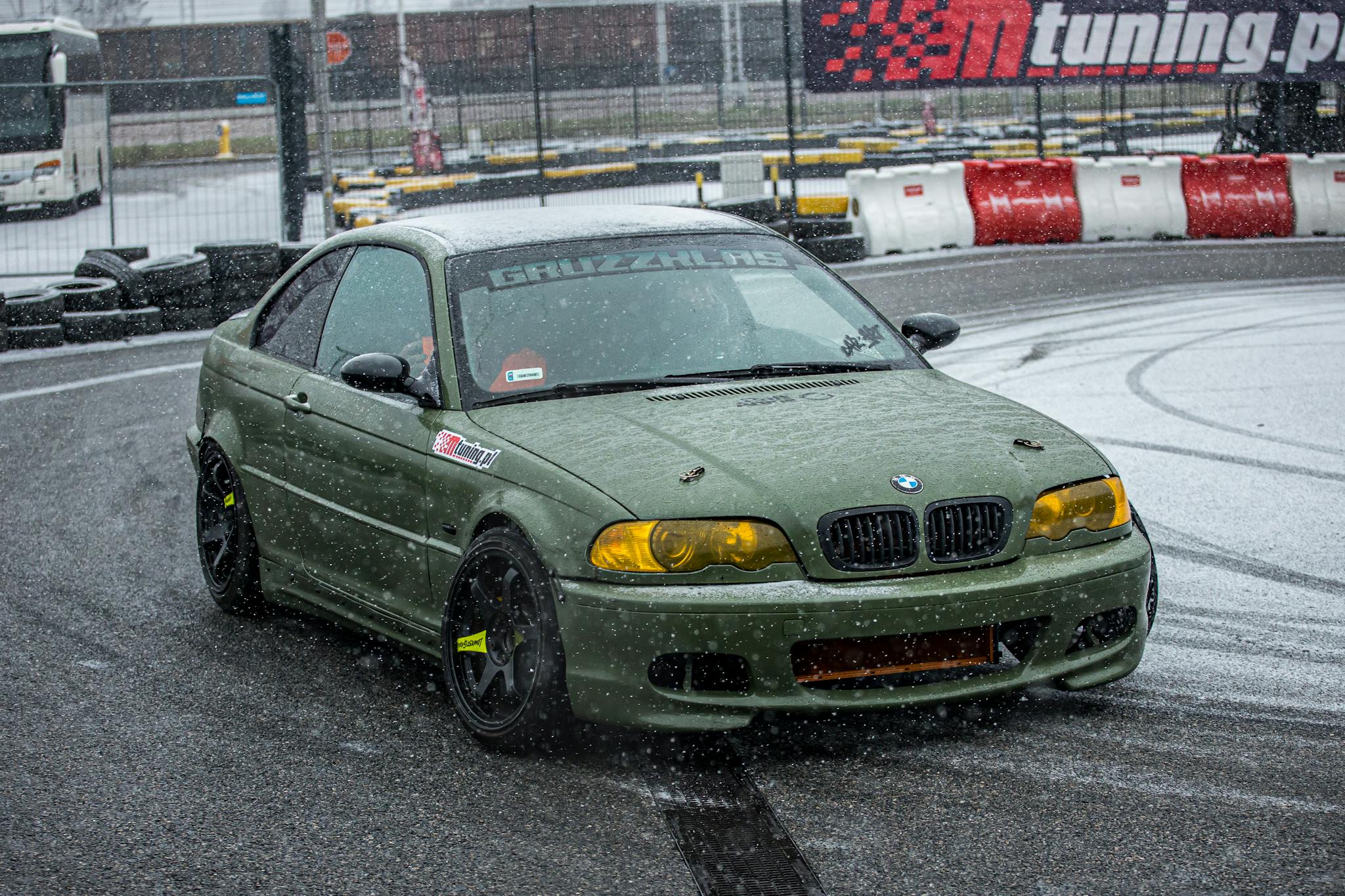 A BMW car drifting on a snowy asphalt track during a motorsport event, showcasing its performance and style.