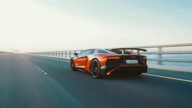 Dynamic shot of a red sports car speeding on an open coastal highway during the day.